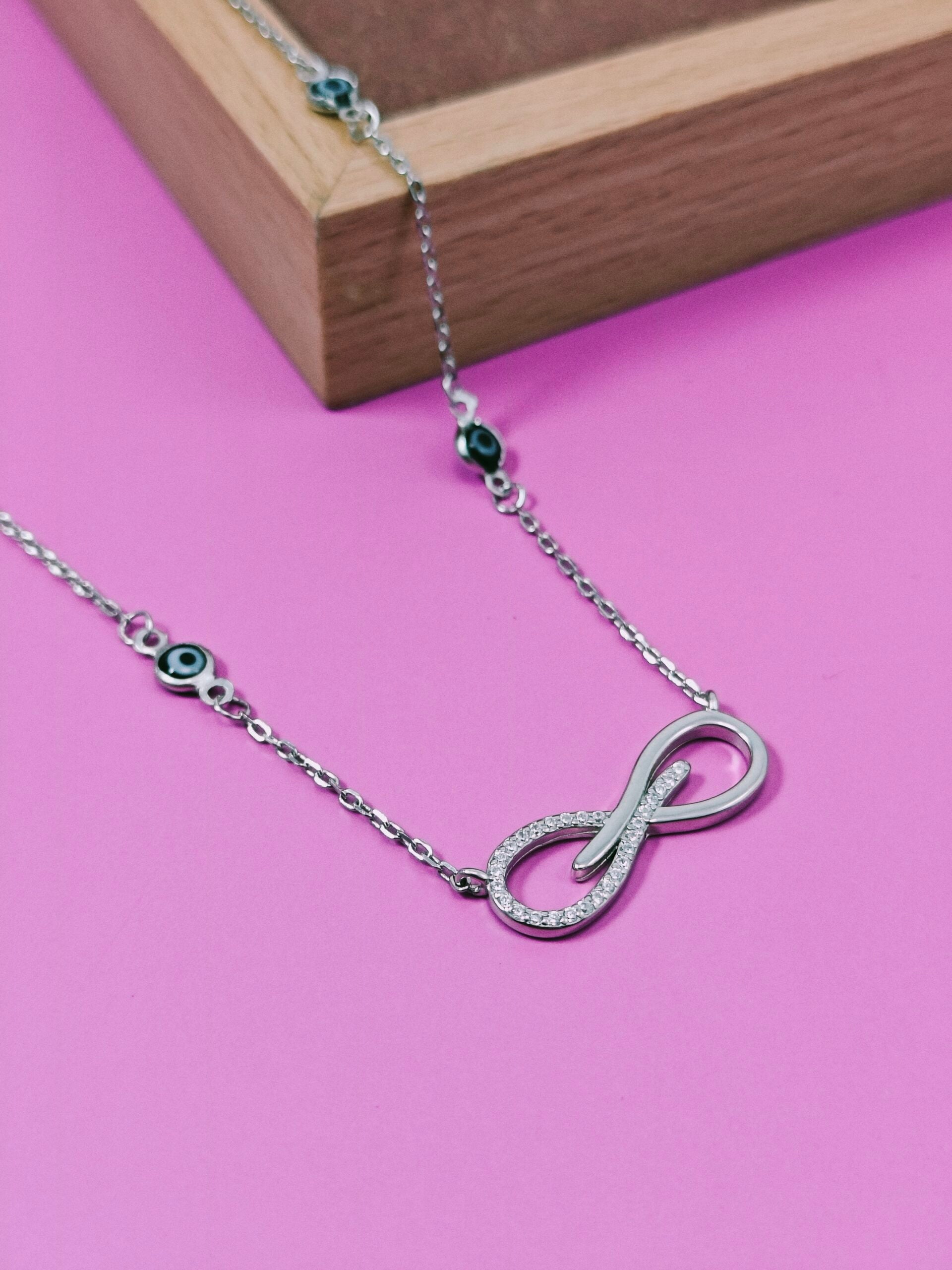 Silver necklace with an infinity symbol pendant on a pink background